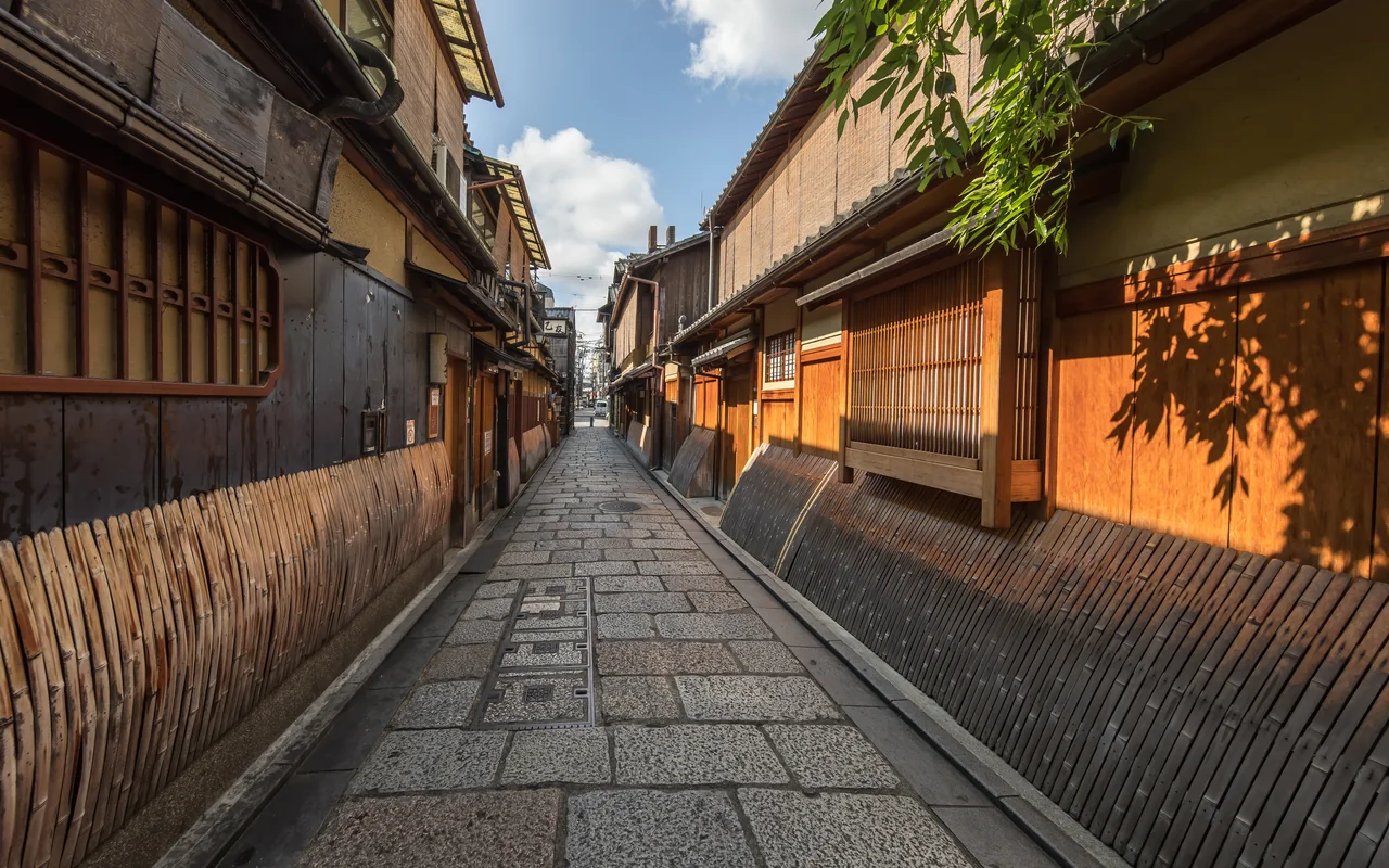 木格子と竹垣の町家が並ぶ、陽の差した祇園の石畳の道。
