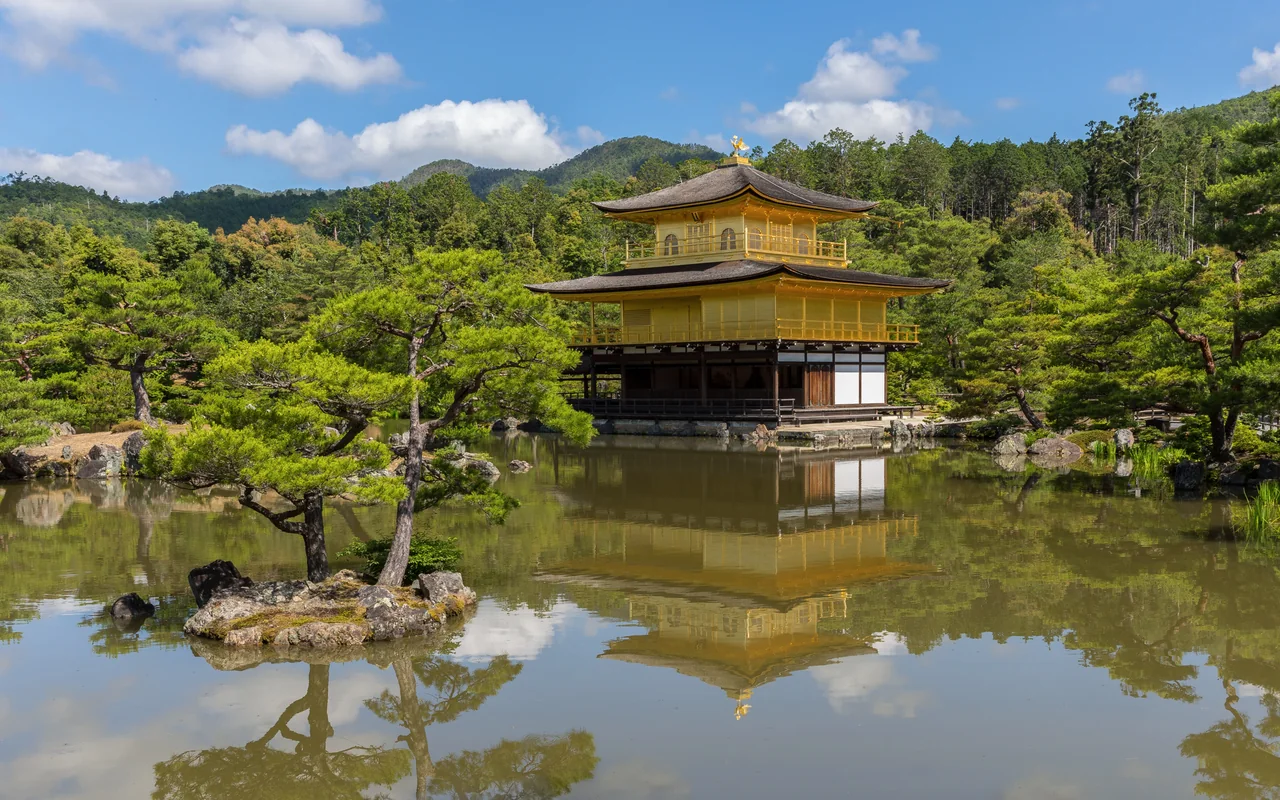青空の下、金閣と周囲の木々が静かな鏡湖池に映っている。